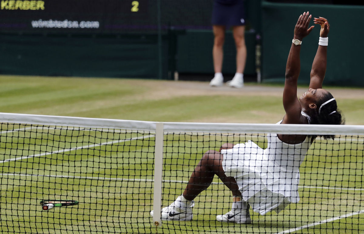 Serena Williamsová padá od radosti na trávu.