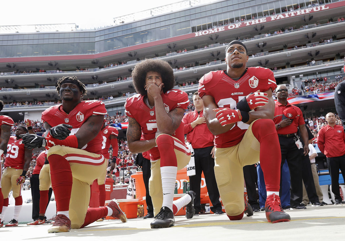 Colin Kaepernick (v strede) pokľakol počas...