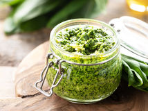Wild leek pesto with olive oil and parmesan cheese in a glass jar on a wooden table. Useful properties of ramson. Leaves of fresh ramson. Horizontal