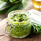 Wild leek pesto with olive oil and parmesan cheese in a glass jar on a wooden table. Useful properties of ramson. Leaves of fresh ramson. Horizontal