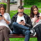 Group of friends two women and one man, sitting on a bench in park separately looking at their phones loosing communication. people using their phones and sending texts as they stand beside each other