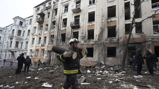 Hasič nesie kusy spíleného stromu pred obytným...