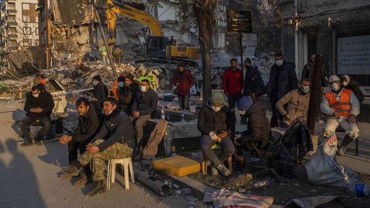 Ľudia sedia vedľa zničeného domu a čakajú na...