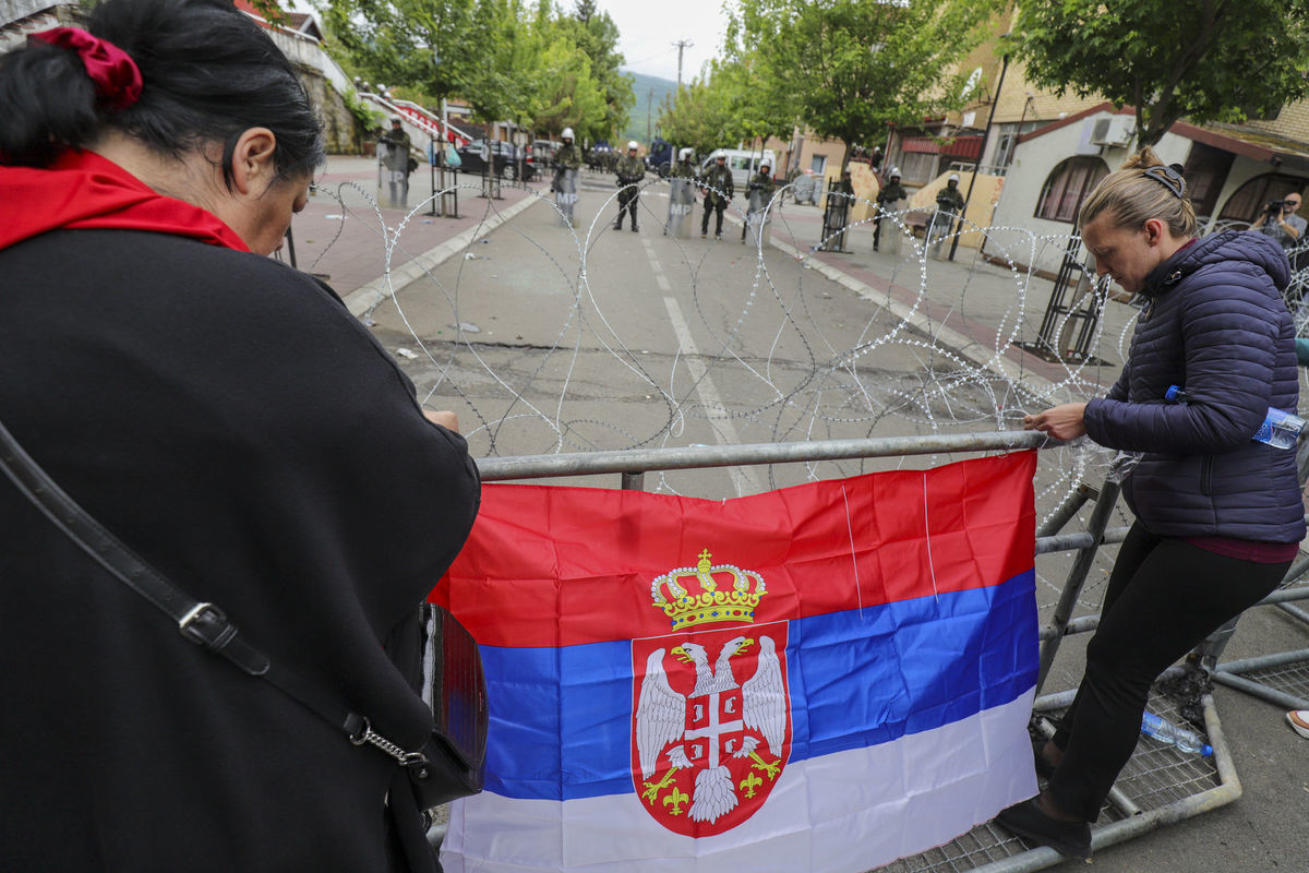Ženy upevňujú srbskú zástavu na oplotenie počas...