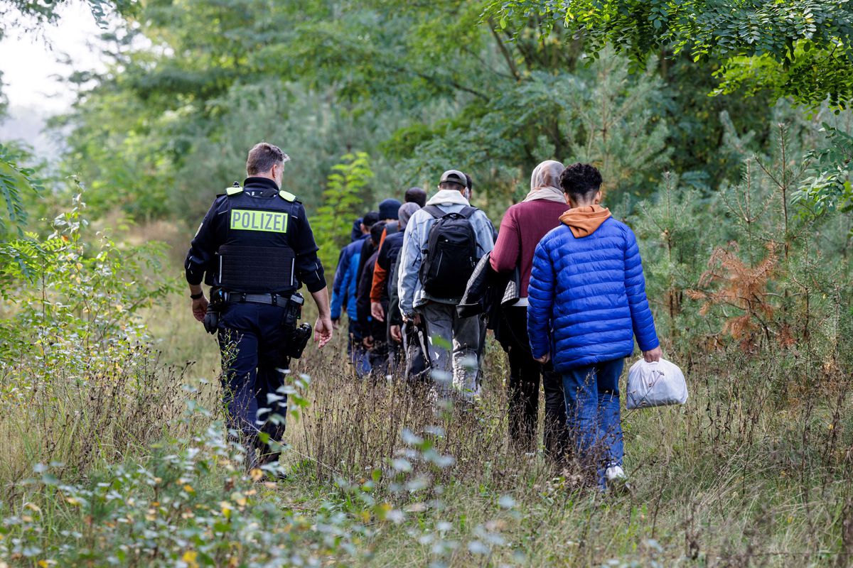 Ein deutscher Polizist nimmt eine Gruppe von Migranten mit...